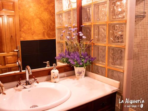a bathroom with a sink and a vase of purple flowers at Alqueria del Hoyo in Cañada del Hoyo
