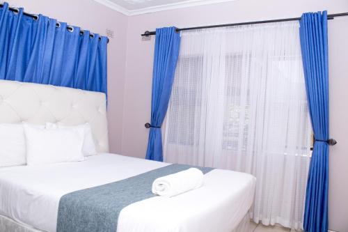 a bedroom with two beds with blue curtains and a window at Villa Prince in Harare