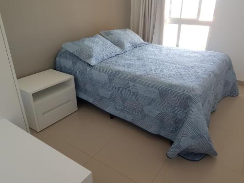 a bedroom with a bed with a blue blanket and a window at Aquiraz Riviera Beach Place Golf Residence in Aquiraz