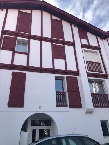 a building with red shuttered windows and a car at Appart 2 pièces avec parking QUARTIER DU LAC in Saint-Jean-de-Luz