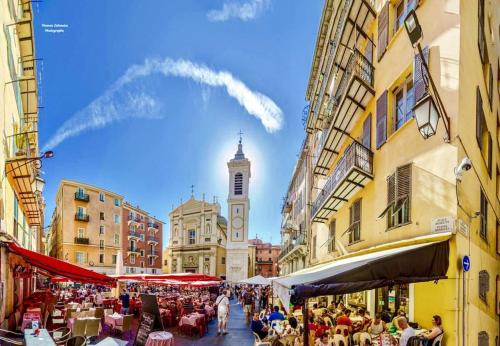 Une foule de personnes assises à des tables dans une rue avec une tour d'horloge dans l'établissement Hyper Centre Place Massena, à Nice