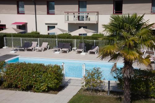 a pool with lounge chairs and a palm tree next to a building at Mercure Dinan Port Le Jerzual in Dinan