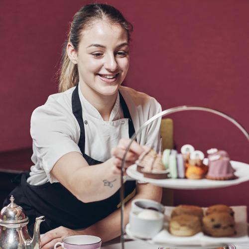 a woman sitting at a table with a tray of desserts at Great Fosters - Near Windsor in Egham