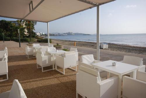 a restaurant with white tables and chairs and the ocean at Hotel Garbi Ibiza & Spa in Playa d'en Bossa