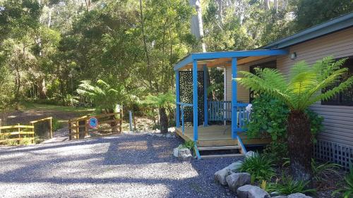 a blue house with a porch and a tree at Strahan Retreat Holiday Park in Strahan
