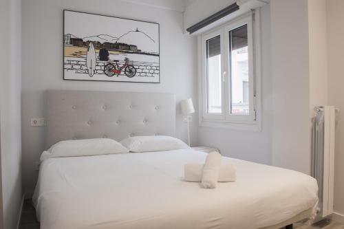 a white bedroom with a large white bed and a window at Plaza B - Local Rentss in San Sebastián