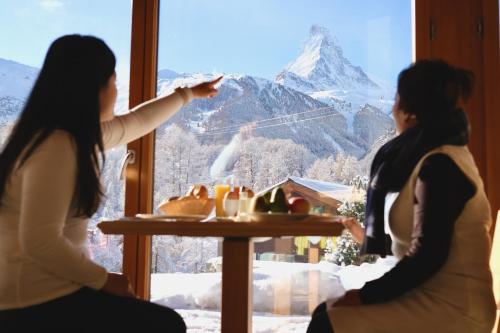 two women looking out of a window at a mountain at Mountain Paradise in Zermatt