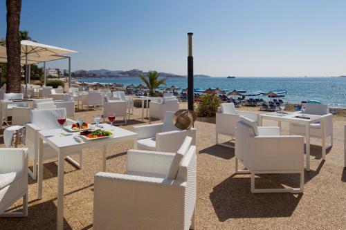 a beach with white chairs and tables and the ocean at Hotel Garbi Ibiza & Spa in Playa d'en Bossa