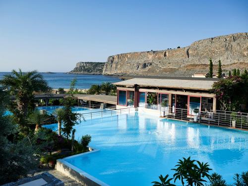 - une piscine d'eau bleue en face d'un bâtiment dans l'établissement Aquagrand Exclusive Deluxe Resort Lindos - Adults only, à Lindos