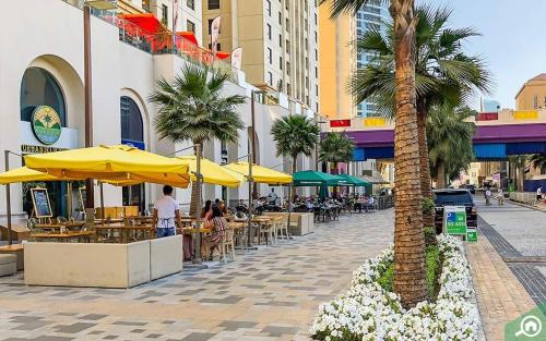 a palm tree on a street with tables and umbrellas at Bombay Backpackers DXB in Dubai