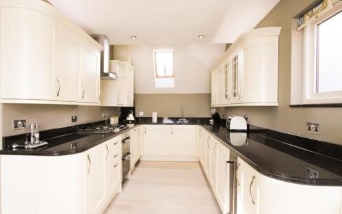 a kitchen with white cabinets and black counter tops at Seagull's Sanctuary in Wells next the Sea