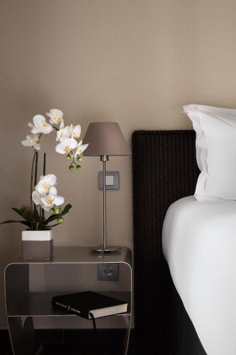a bed with a table with a lamp and white flowers at Le Pinarello in Sainte-Lucie de Porto-Vecchio