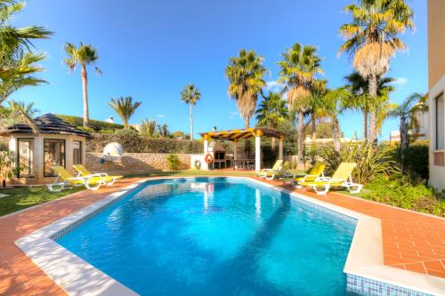 a swimming pool with chairs and palm trees at Vivenda Alegria in Albufeira
