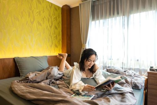 a woman laying in bed reading a book at Tepbunthom Hostel in Bangkok
