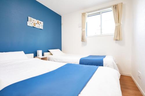 2 camas en una habitación con paredes azules y ventana en E-horizon Resort コンドミニアム名護 A, en Nago