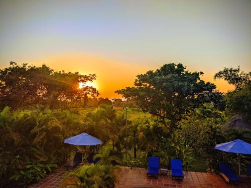 a sunset over a patio with blue chairs and umbrellas at Raingsey Bungalow in Kep