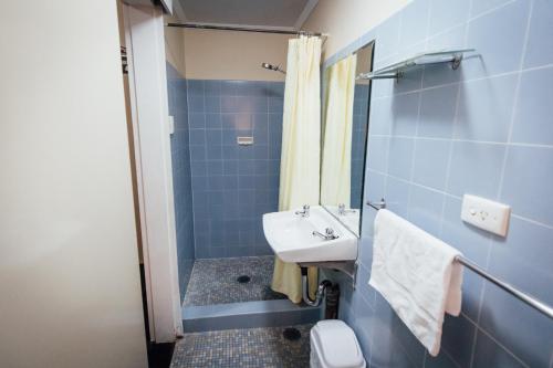 La salle de bains bleue est pourvue d'un lavabo et d'une douche. dans l'établissement Shortland Budget Accommodation, à Jesmond