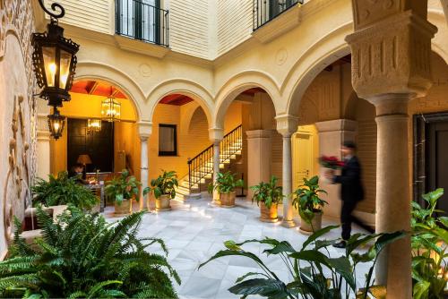 Casa de Triana Luxury Suites by Casa del Poeta في إشبيلية: امرأة تسير في مبنى به نباتات الفخار