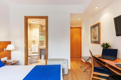 a room with a bed and a desk with a laptop at Sercotel de los Reyes in San Sebastián de los Reyes