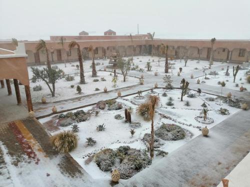 a courtyard covered in snow with palm trees and bushes at Hotel Meteorites Boulaajoul in Zaida