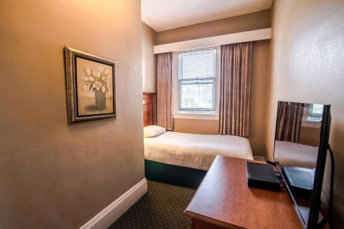 a hotel room with a bed, desk and a painting on the wall at The Sylvia Hotel in Vancouver