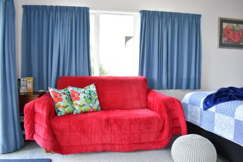 a red chair in a room with blue curtains at Hibiscus Bed & Breakfast in Waihi Beach