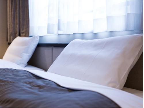 a bed with white pillows sitting next to a window at THE HOTELS HAKATA KASANE Bayside in Fukuoka