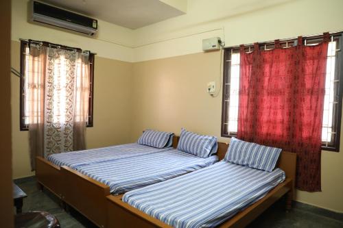 2 Betten in einem Zimmer mit 2 Fenstern in der Unterkunft R. VE. R Residency in Thanjavur