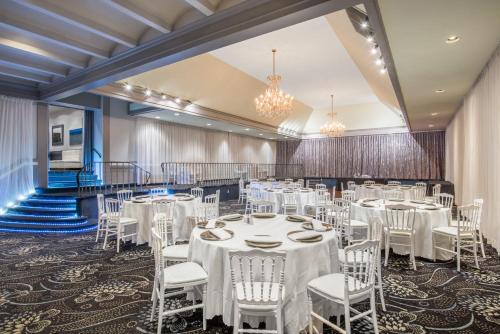 une salle de banquet avec des tables blanches, des chaises et des lustres dans l'établissement Armon Plaza Montreal Airpt, Trademark Collection by Wyndham, à Montréal