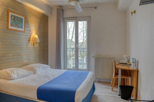 a bedroom with a bed and a desk and a window at Hotel Le Gambetta in Bergerac