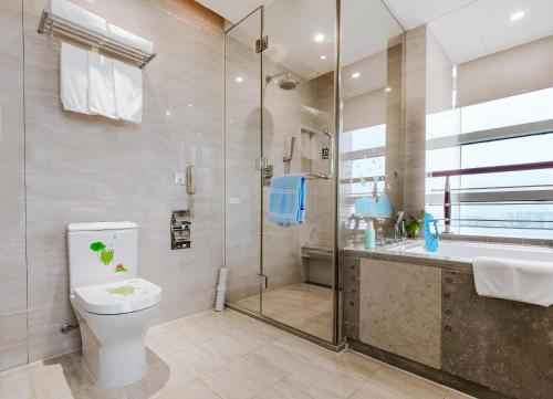 a bathroom with a toilet and a shower and a sink at New Century Hotel Qingdao in Huangdao