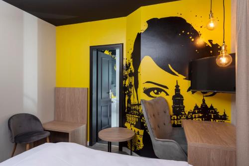 a bedroom with a yellow wall with a painting on it at ibis Styles Dresden Neustadt in Dresden