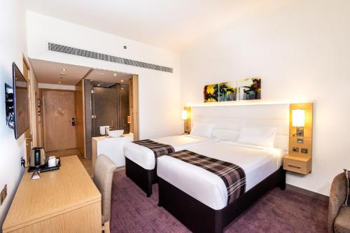 a hotel room with two beds and a desk at Premier Inn Dubai Dragon Mart in Dubai