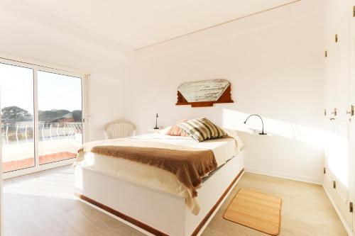 a white bedroom with a bed and a window at Espectacular apartamento na praia a 20 min de Lisboa in Costa da Caparica