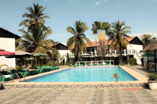 a pool with palm trees and a person in the water at Bungalow Beach Hotel in Serekunda