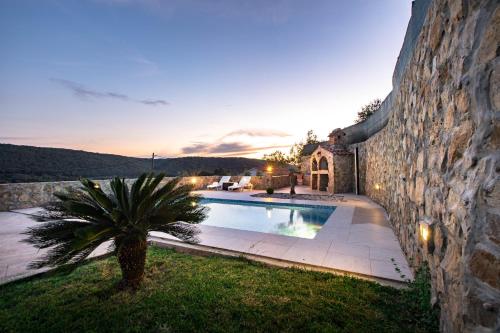 a villa with a swimming pool next to a stone wall at Apartments Bajcic in Rab