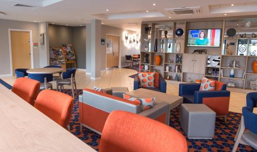 Holiday Inn Express Dunfermline, an IHG Hotel في دنفرملاين: غرفة انتظار مع كراسي وطاولات برتقالية وزرقاء