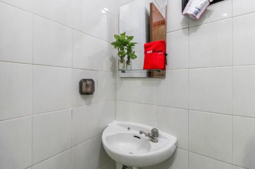 a white tiled bathroom with a sink and a plant at RedDoorz Plus near Trisakti University in Jakarta