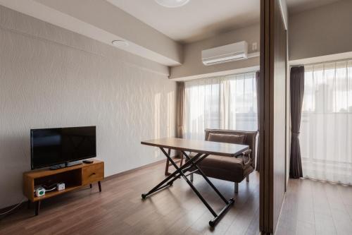 Habitación con mesa, TV, mesa y sillas. en Ostay Shin-Osaka Hotel Apartment en Osaka