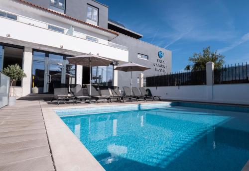 卡帕里卡海岸的住宿－Villa Caparica Hostel，一座带椅子和遮阳伞的游泳池位于一座建筑旁边