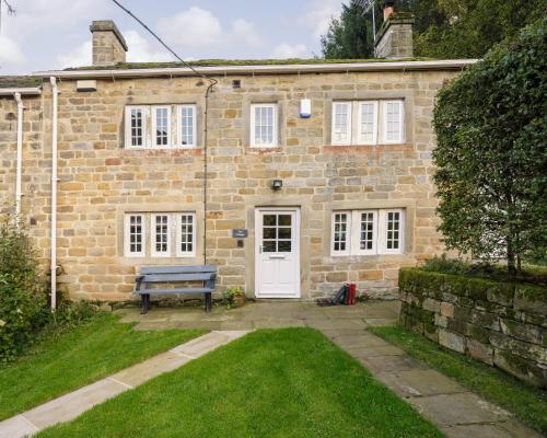 a stone house with a blue bench in front of it at Carr Cottage in Leeds