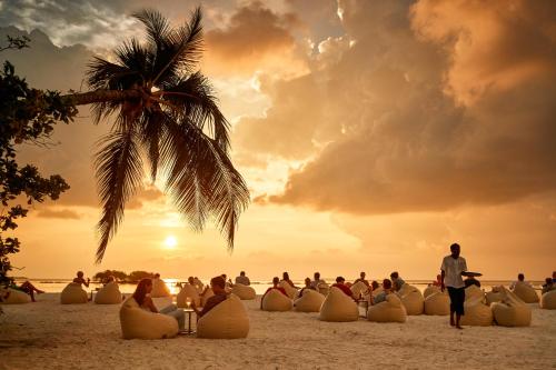 a group of people sitting on the beach watching the sunset at ROBINSON NOONU - All Inclusive in Manadhoo