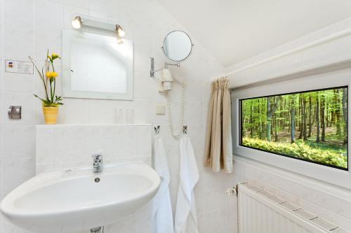 a white bathroom with a sink and a window at Restaurant & Hotel Baumhaus Hagen in Sassnitz