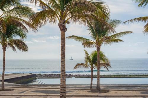 Castillo del Romeral的住宿－APARTAMENTOS BLUE EYES，两棵棕榈树,在海洋前,有一艘帆船