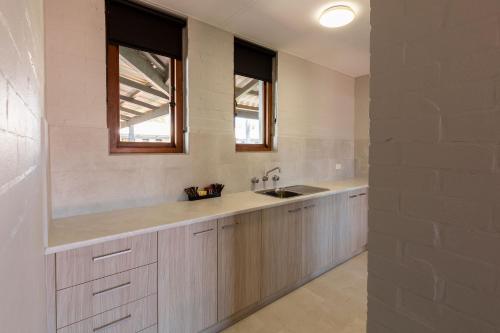 a kitchen with white cabinets and a sink and two windows at Nightcap at Wintersun Hotel in Geraldton