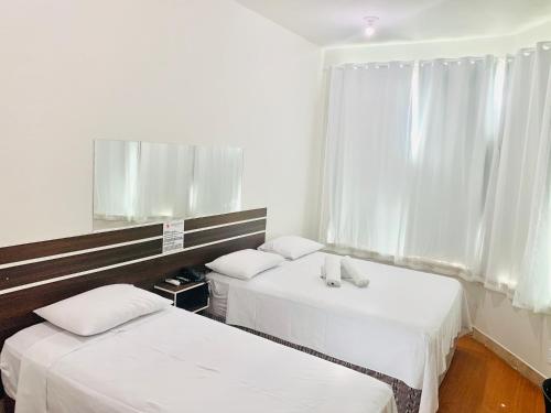 two beds in a room with white walls and a window at SAMIR HOTEL COMFORT in Porto Velho