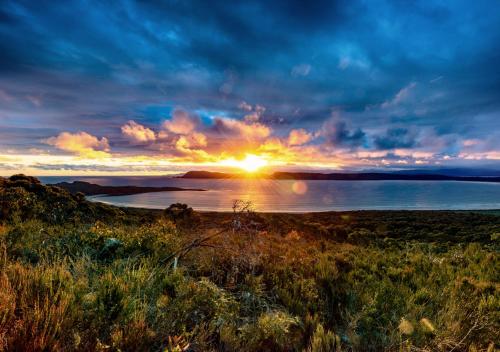 a sunset over a body of water with the sun setting at Cloudy Bay Cabin in South Bruny