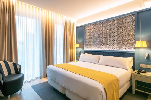 a hotel room with a large bed and a chair at Catalonia Porto in Porto