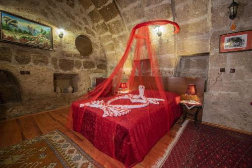 a bedroom with a red bed in a stone room at Kapadokya Ihlara Konakları Otel Konak Odaları in Guzelyurt