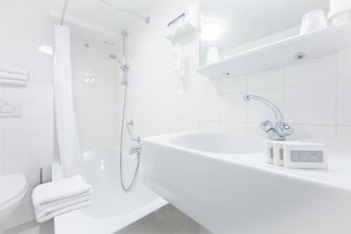ein weißes Bad mit einer Dusche und einem Waschbecken in der Unterkunft Hotel Residence Le Coin in Amsterdam